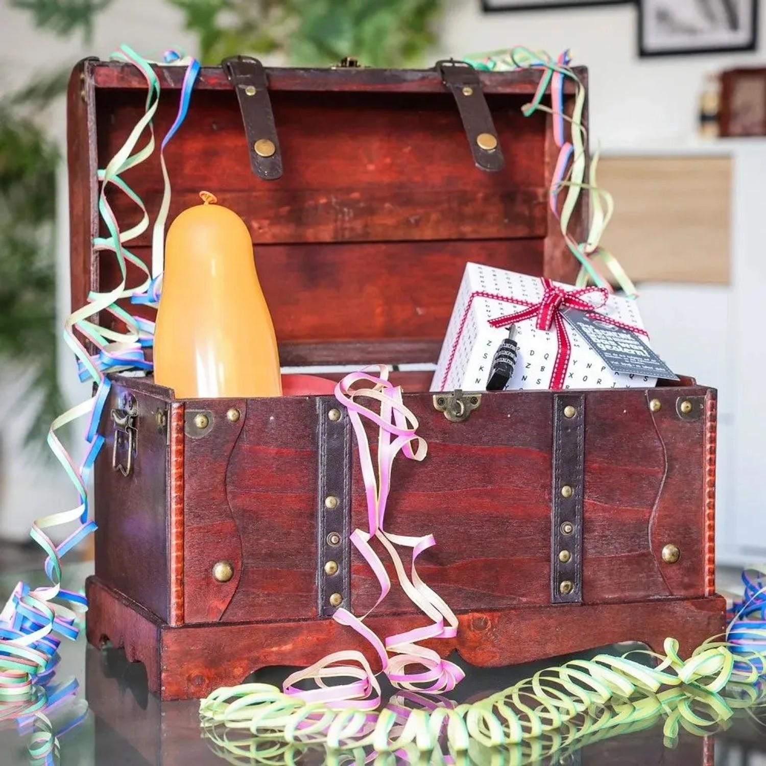 Offene HMF Holztruhe im Vintage-Stil, dunkelbraun, mit Geschenk und Ballon, umgeben von bunten Partybändern. Ideal zur Aufbewahrung.