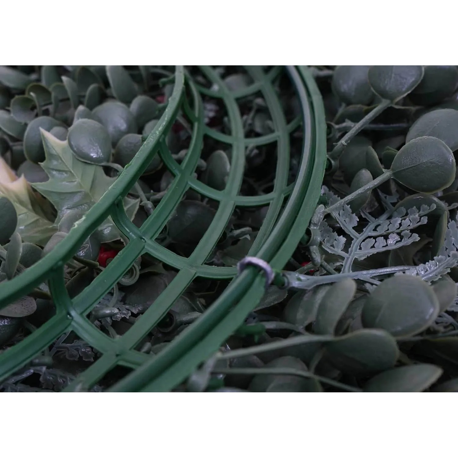 Detailansicht des künstlichen Weihnachtskranzes: grüne Polyethylen-Basis mit Blättern und roten Beeren.