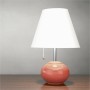 Moderne Tischlampe mit weißem, konischem Schirm und glänzendem, runden, korallfarbenen Fuß auf Holztisch.