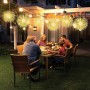 Leuchtende Pusteblumen-LED-Kugeln als Weihnachtsdekoration erhellen eine Terrasse. Warmweißes Licht schafft festliche Stimmung beim Abendessen.