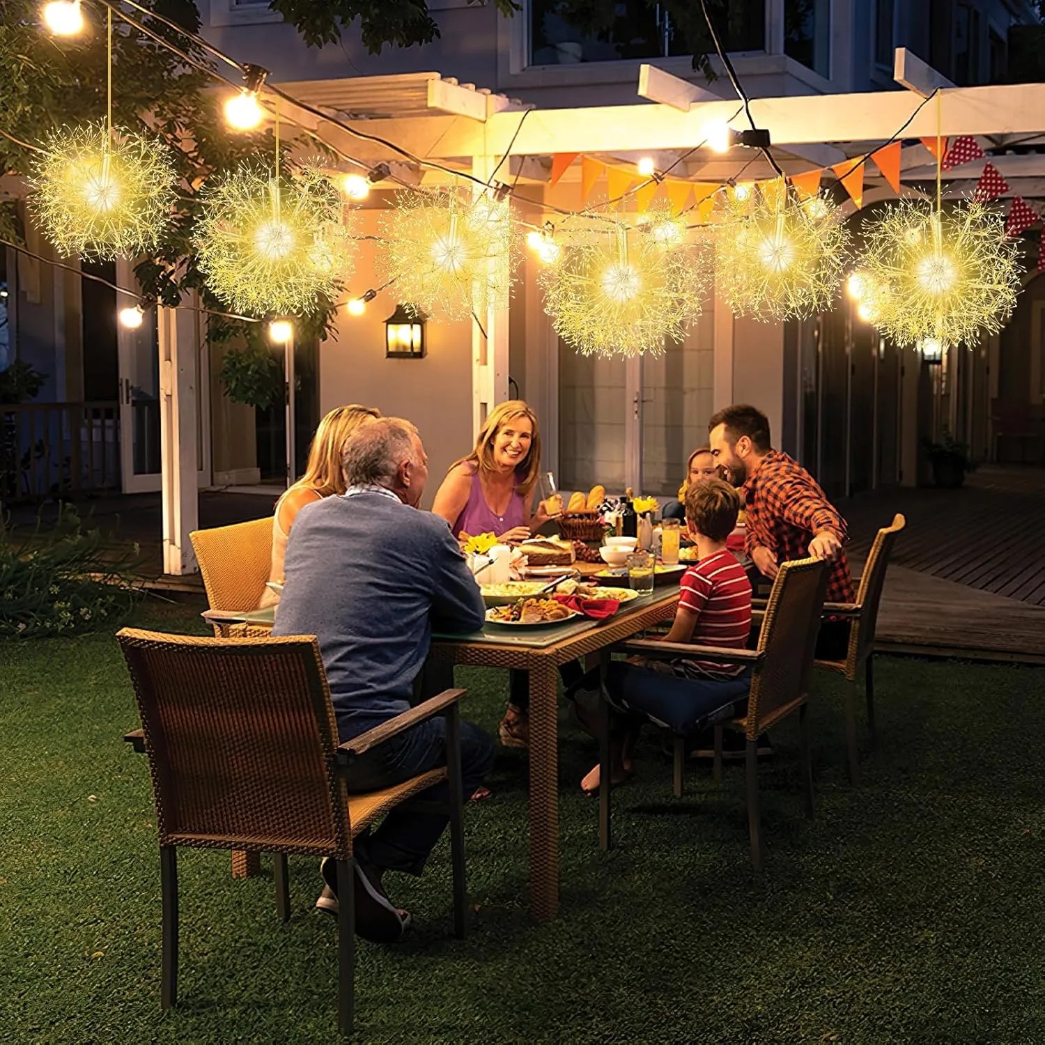Leuchtende Pusteblumen-LED-Kugeln als Weihnachtsdekoration erhellen eine Terrasse. Warmweißes Licht schafft festliche Stimmung beim Abendessen.