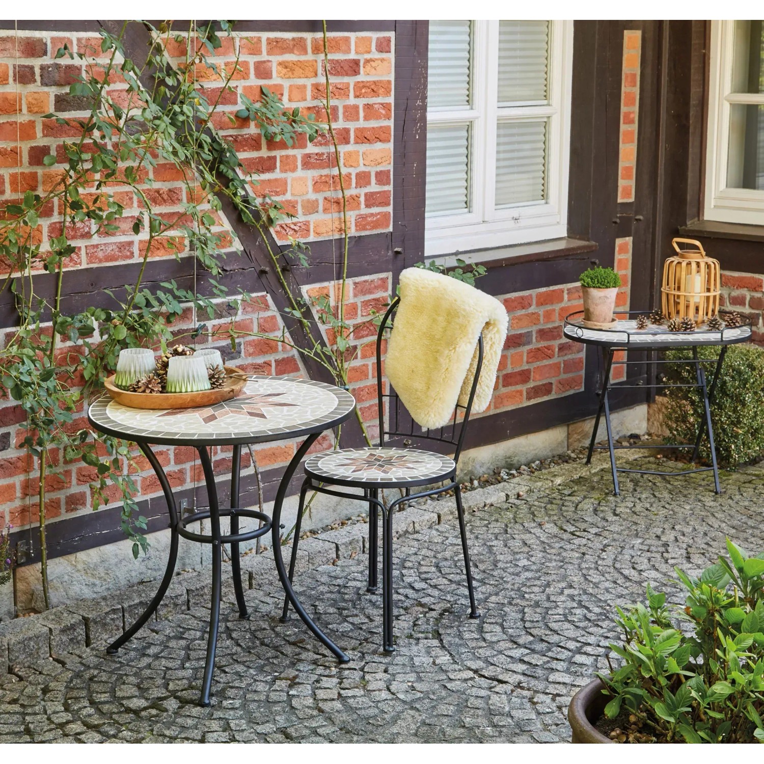 Runder, grauer Siena Garden Gartentisch Stella (Ø 70 cm) mit Stuhl auf einer Terrasse.