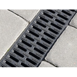 Schwarze ACO Hexaline 2.0 Entwässerungsrinne aus Kunststoff mit Microgrip Rost zwischen Pflastersteinen.