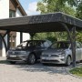Skan Holz Carport Friesland schiefergrau mit Flachdach und Einfahrtsbögen, zwei Autos darunter.