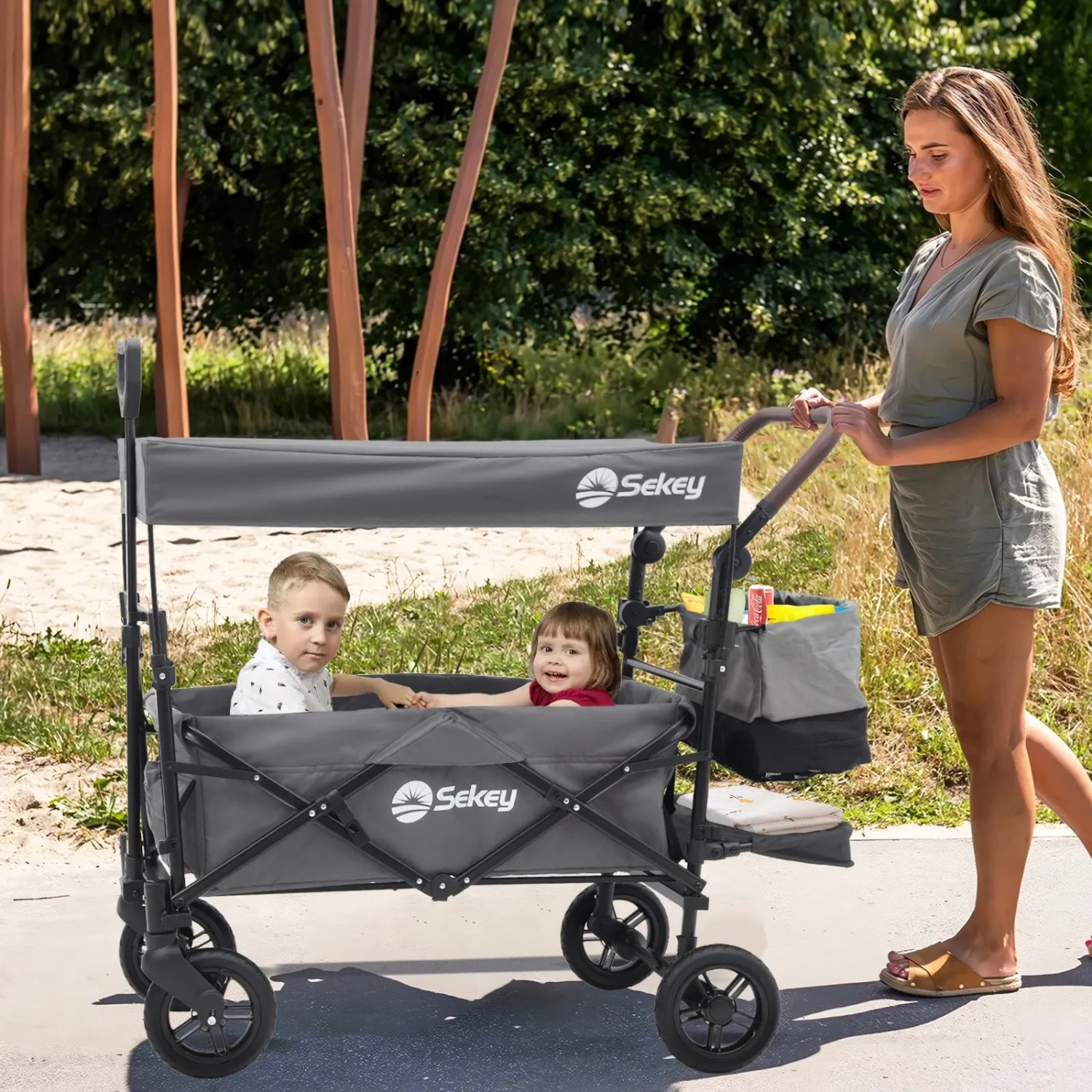 Sekey Bollerwagen mit Dach, grau, mit zwei Kindern und schiebender Frau. Ideal für Camping und Ausflüge.