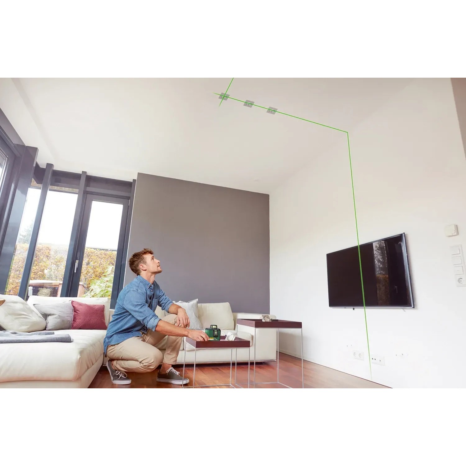 Mann nutzt Bosch AdvancedLevel 360 Kreuzlinienlaser zur Ausrichtung im Wohnzimmer.