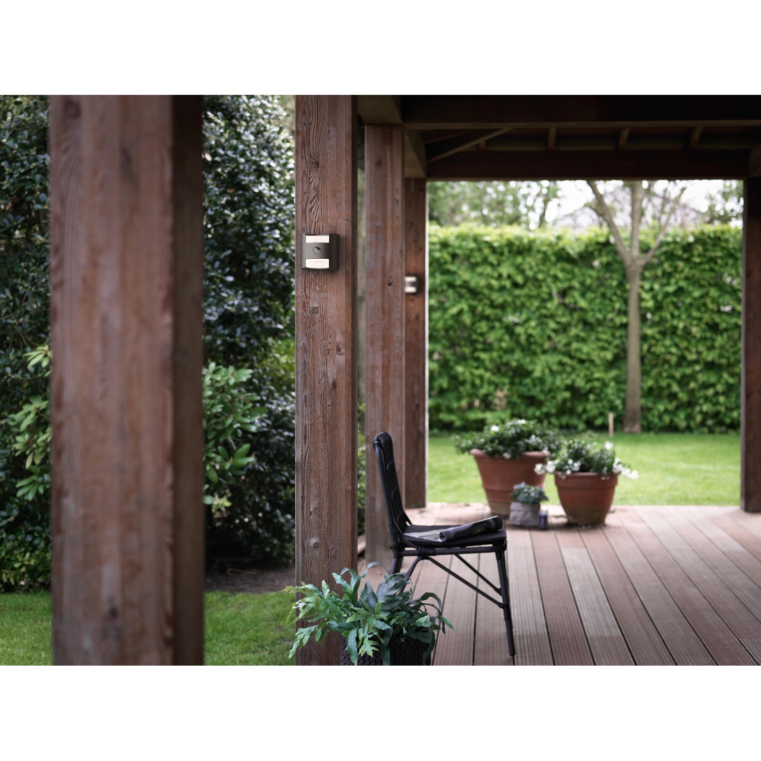 Anthrazitfarbene Philips LED-Außenwandleuchte Grass mit Bewegungsmelder an Holzpfosten.