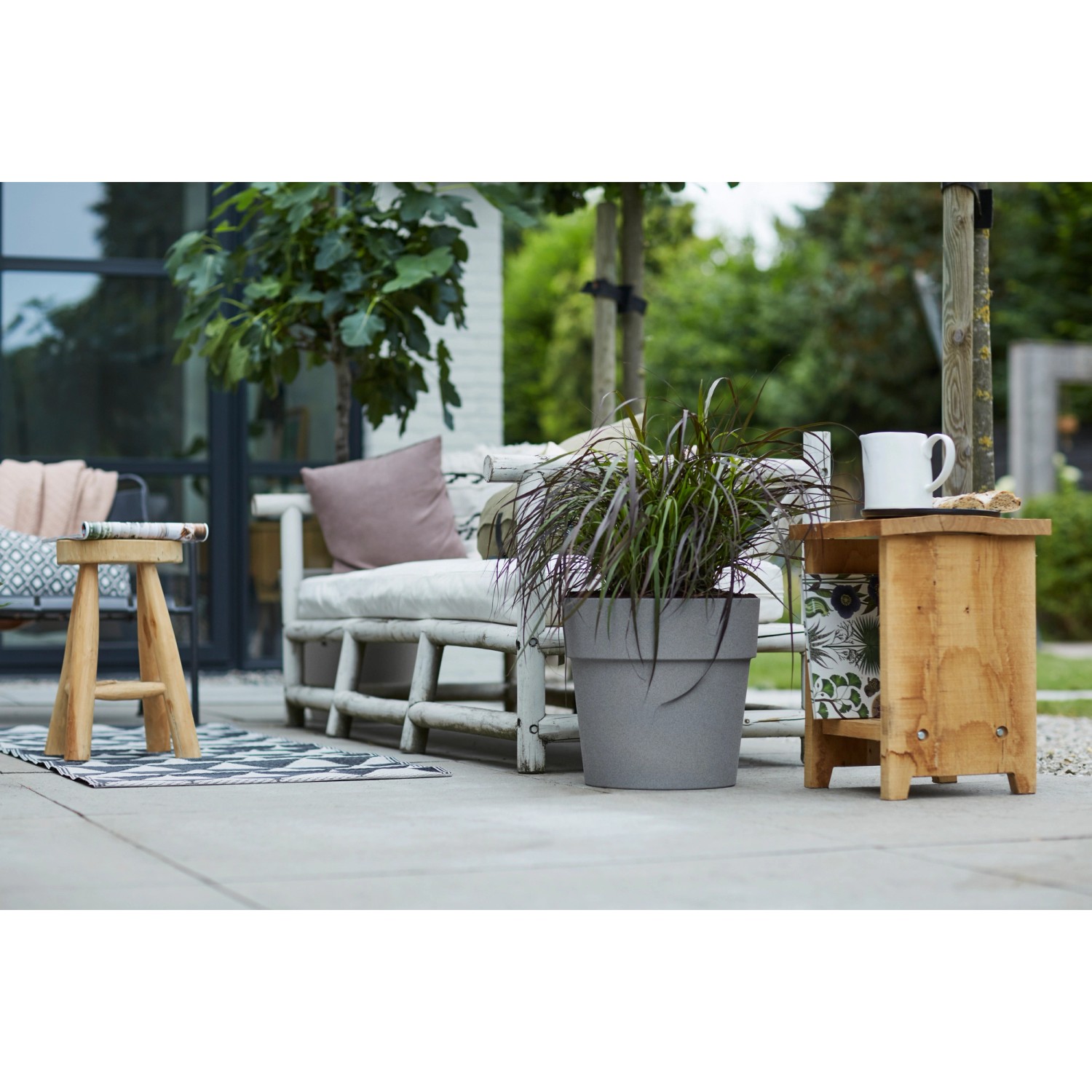 Grauer Elho Blumentopf Vibia Straight Living Beton, Ø 25 cm, mit Pflanze im Garten.