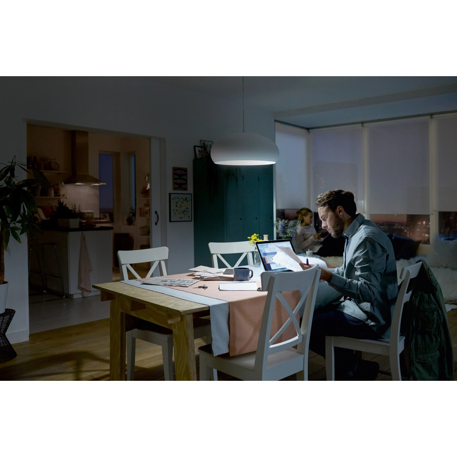 Philips LED-Lampe E27, 6,5W, neutralweiß im Einsatz über Esstisch mit Person am Laptop.