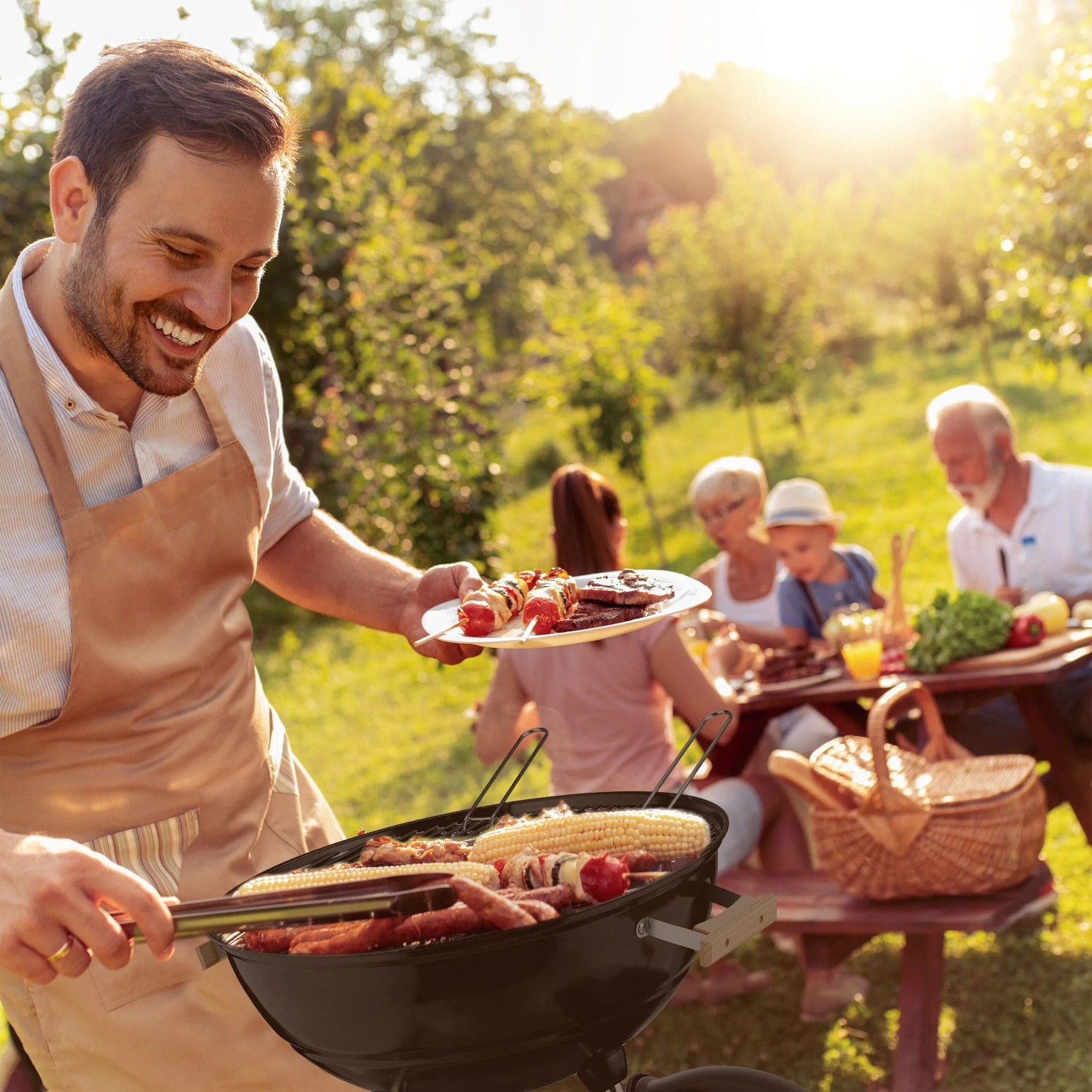Mann grillt auf schwarzem Relaxdays XL Kugelgrill im Garten. Würstchen, Mais, Spieße auf dem Rost. Familie genießt BBQ.