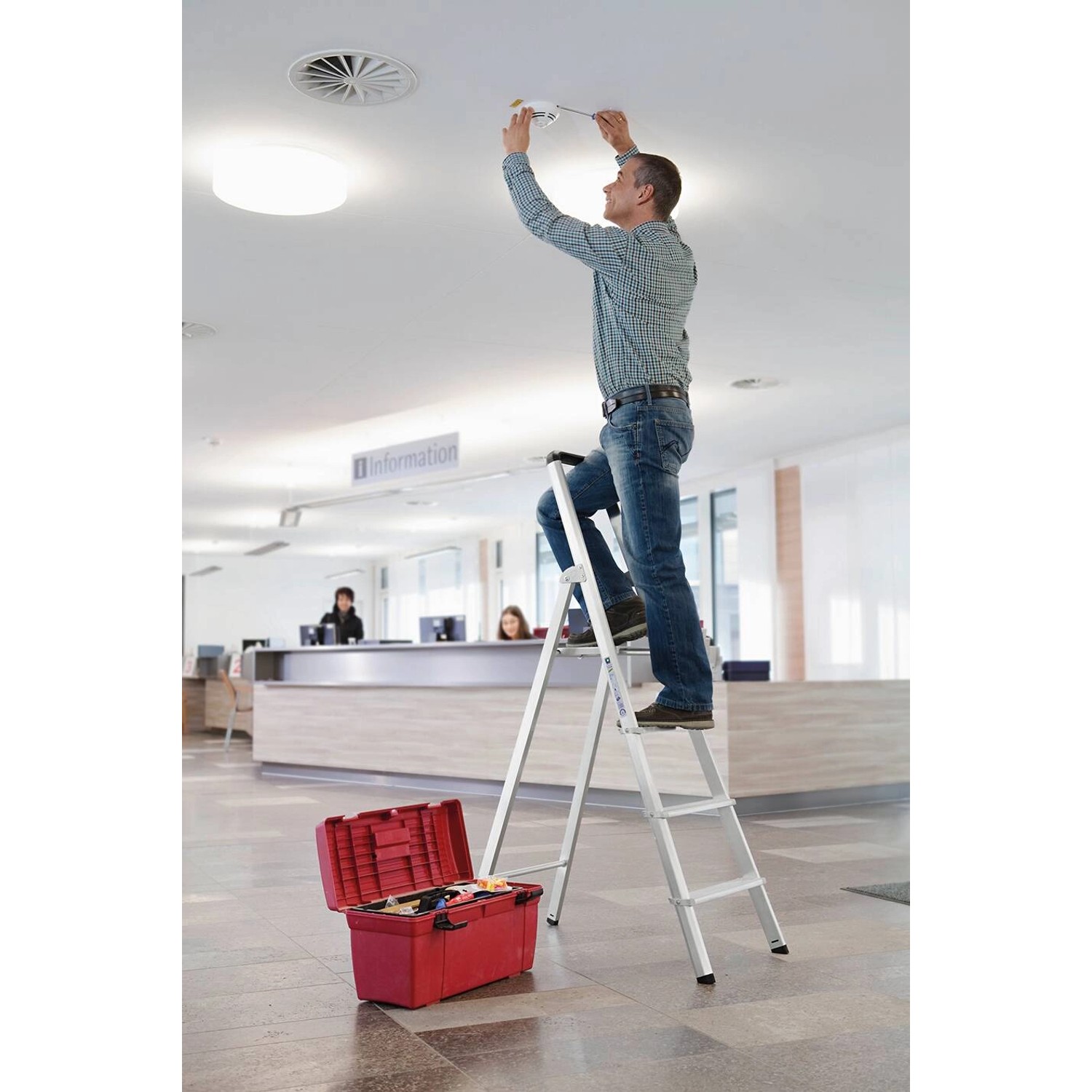 Mann auf PROREGAL Stufen-Stehleiter (3 Stufen) bei Reparatur. Werkzeugkiste im Vordergrund.