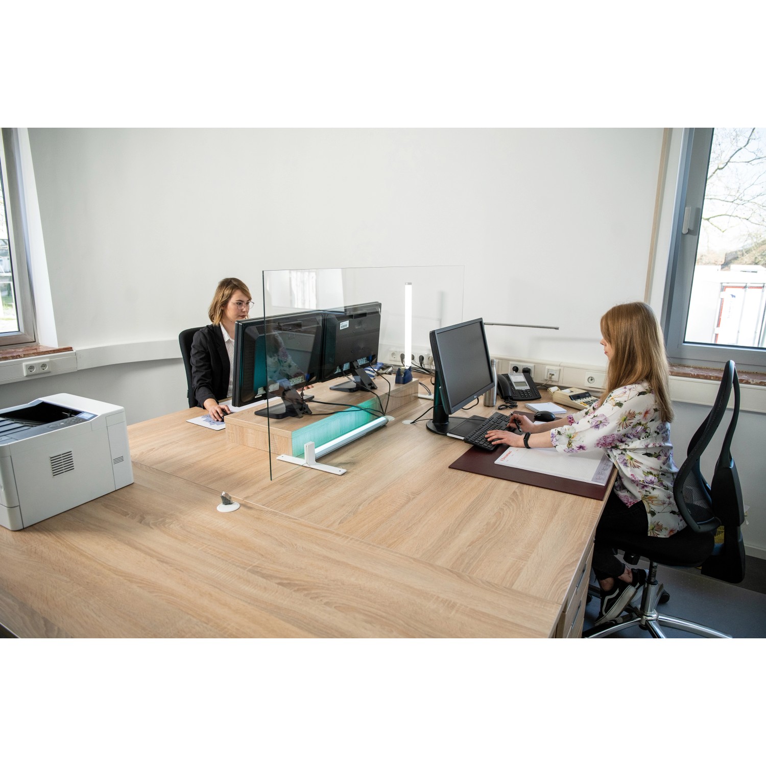 Hygiene Schutzglas Klarglas 600x500 mm auf Schreibtisch mit zwei Personen im Büro.