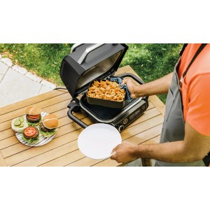 Ninja Woodfire Crisper-Korb auf Grill mit Curly Fries und Burgern im Hintergrund.