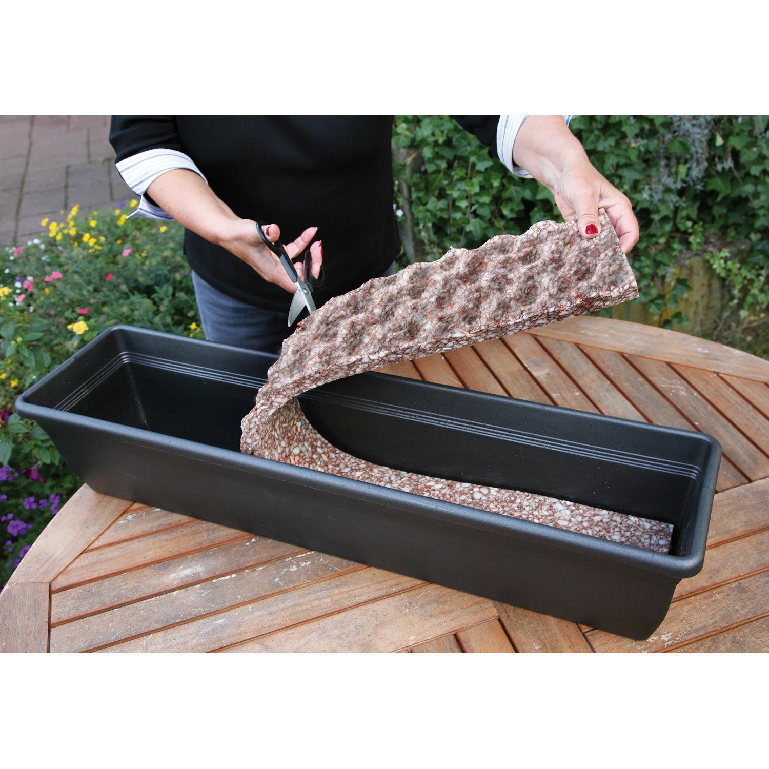 Floraworld Wasserspeichermatte wird mit einer Schere für einen Blumenkasten zugeschnitten.