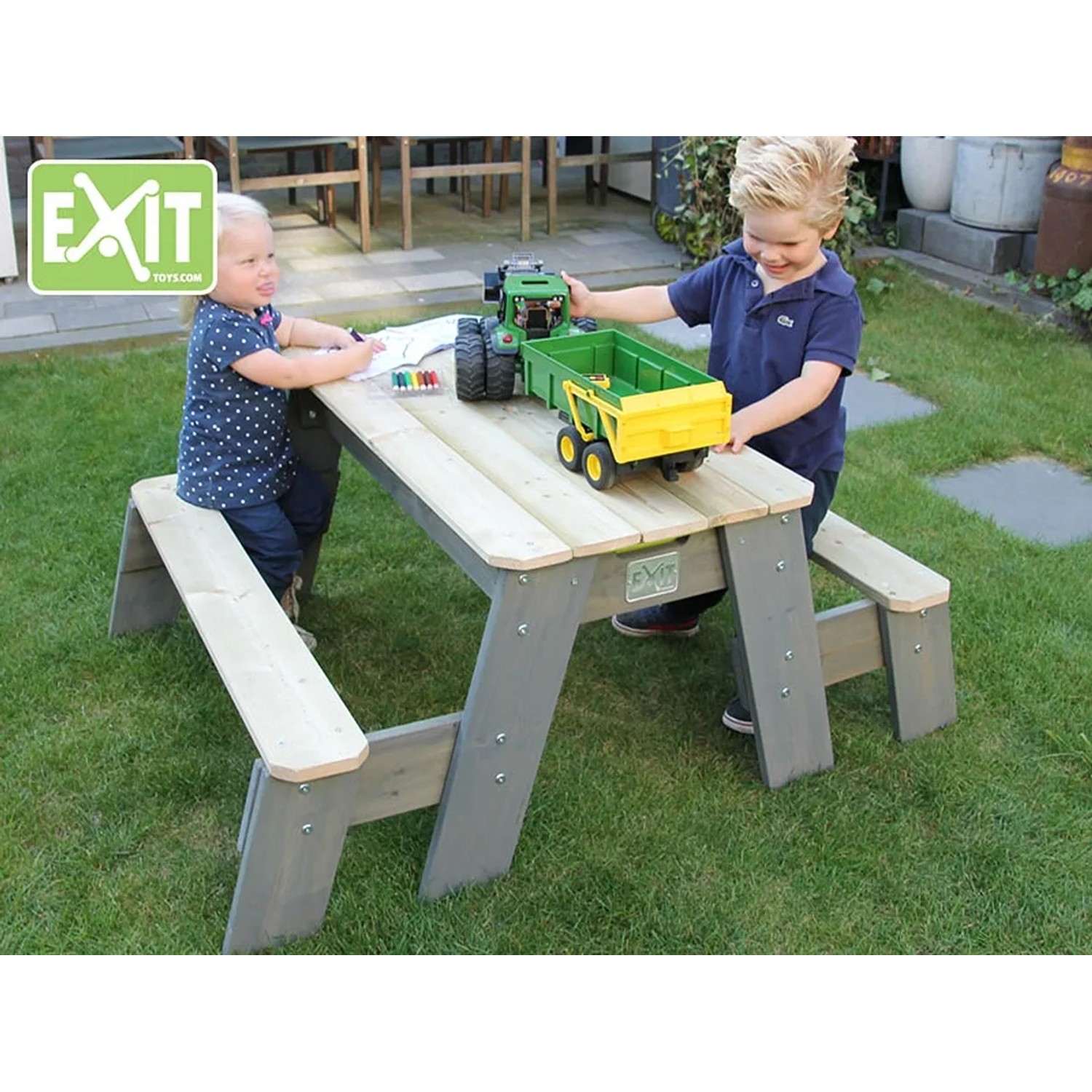 EXIT Aksent Sand-, Wasser- und Picknicktisch mit 2 Bänken im Garten mit spielenden Kindern.