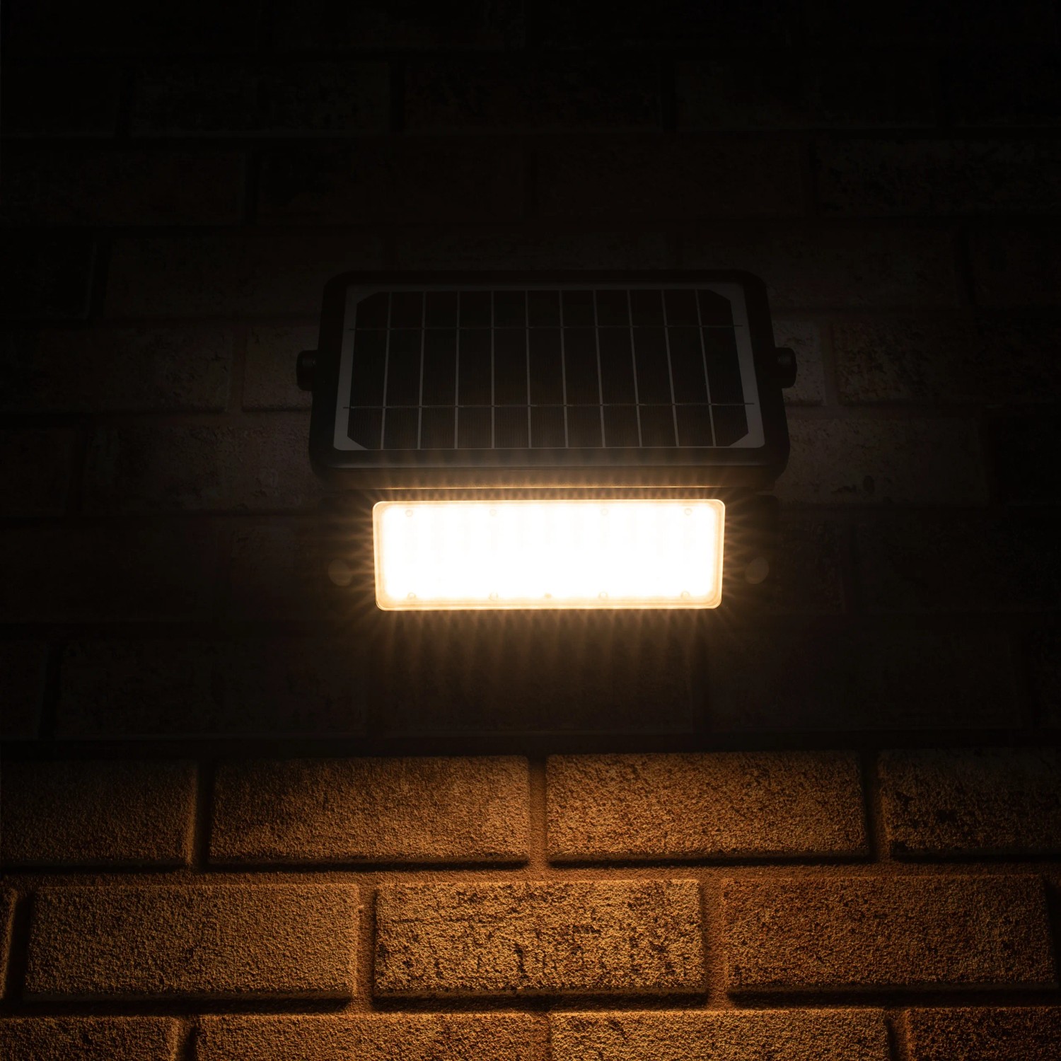 Schwarze LED Solar-Außenleuchte mit Sensor, 10W, 1080lm, 3000K an einer Backsteinwand.