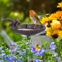 Braune Gusseisen Vogeltränke mit Dekovogel im Garten. Ein Rotkehlchen sitzt auf der Muschelschale mit Erdspieß.