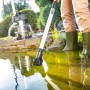 Teichschlammsauger 2.0 Edelstahl im Einsatz zur Teichreinigung. Person mit Gummistiefeln steht im Wasser.