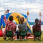 Person hält braunen Relaxdays Flachmann aus Edelstahl mit Kunstlederhülle beim Camping am See.