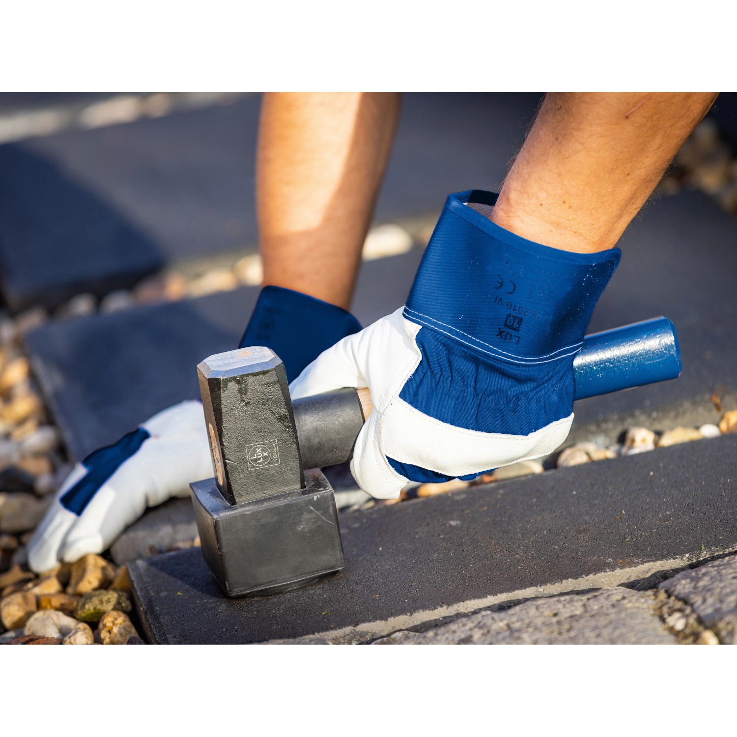 Hände mit LUX Arbeitshandschuhen (Gr. 10) verlegen Pflastersteine mit Hammer.