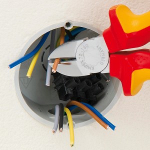 Knipex Seitenschneider 160 mm schneidet Draht in Verteilerdose. Zange mit Chrom-Finish und rot-gelben Griffen.