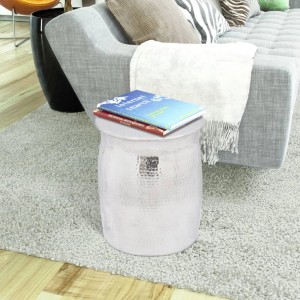 Silberner Hocker/Beistelltisch aus gehämmertem Aluminium mit Büchern, neben grauem Sofa auf hellem Teppich.