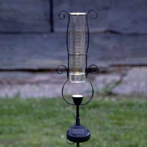 LED-Solar-Regenmesser mit schwarzem Metallgestell, Messglas und leuchtender LED im Garten. Solar-Deko.