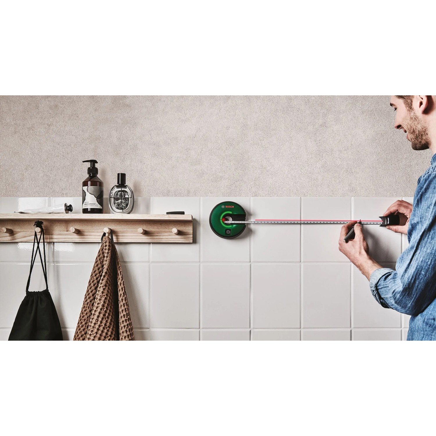Bosch Atino Linienlaser mit Maßband im Einsatz an weißer Wand.