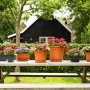 Verschiedene bepflanzte Blumenkästen und Blumentöpfe (Florus) in Braun- und Anthrazittönen auf einem Gartentisch.