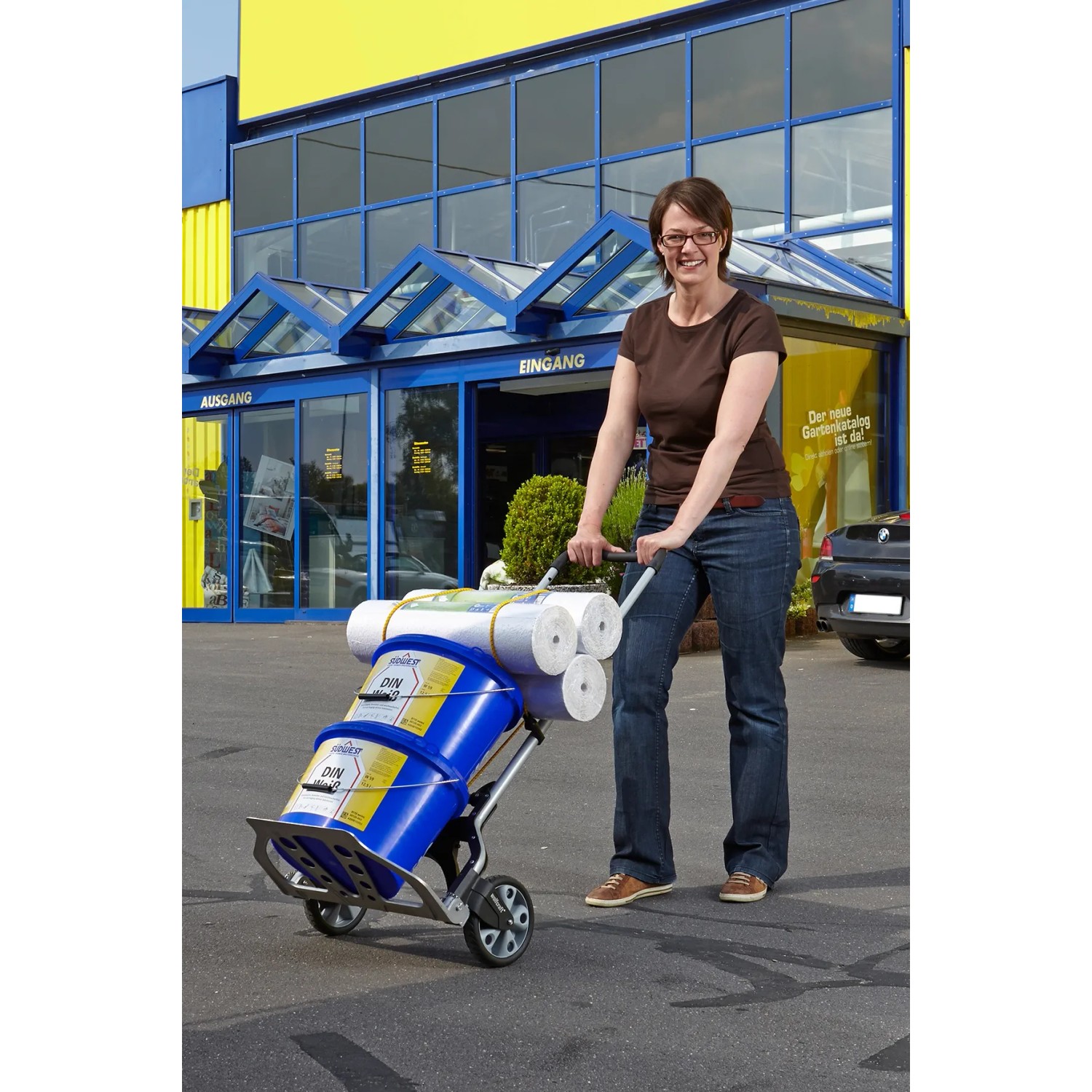 Frau transportiert Farbeimer und Rollen mit der klappbaren wolfcraft Sackkarre TS 850 (100 kg) vor dem OBI Markt.