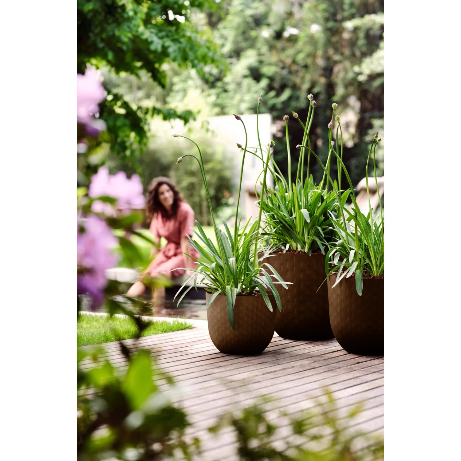 Elho Blumentopf Fuente Grains, Ø 30 cm, rostbraun, mit Pflanzen auf Holzterrasse.
