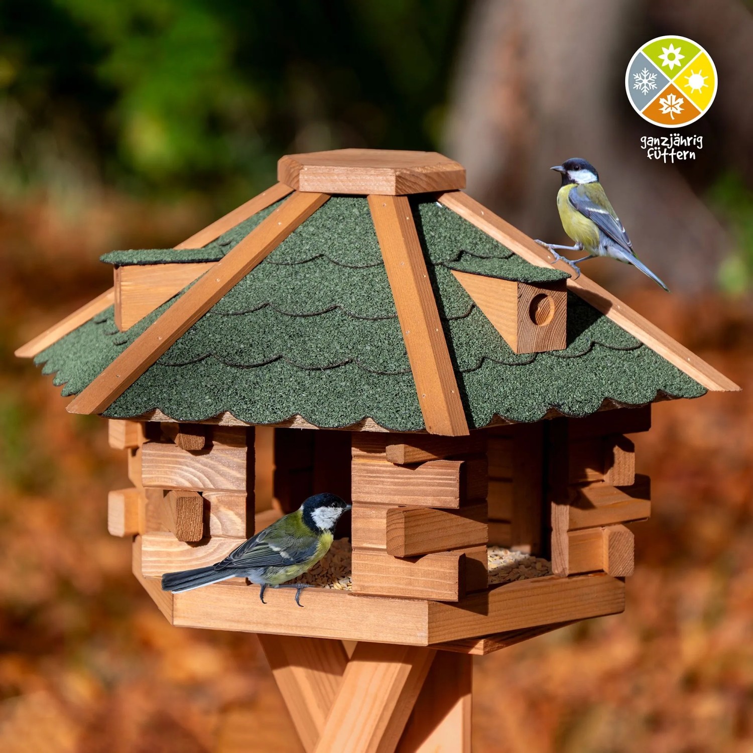 Sechseckiges Dobar Vogelhaus aus Holz mit grünem Bitumendach. Zwei Meisen fressen am Futterhaus.