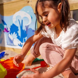 Mädchen spielt im Sandkasten des pastellblauen Wickey Disney Adventure Spielturms.