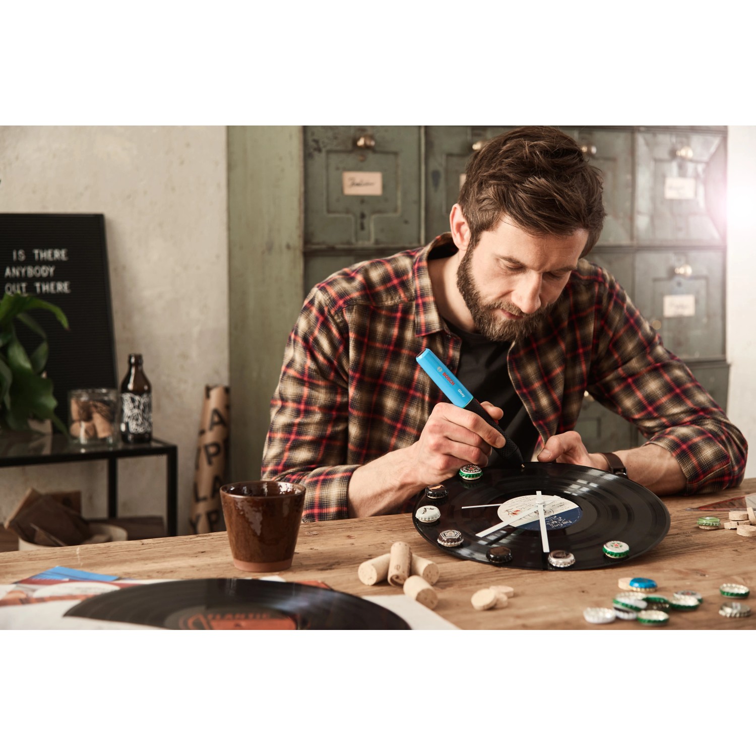 Mann klebt mit blauem Bosch Gluey Heißklebestift Deko auf Schallplatte. Heißklebegerät für Bastelprojekte.