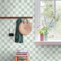 Grüne Vliestapete mit Karomuster an einer Wand, dekoriert mit Garderobe und Blumen am Fenster.