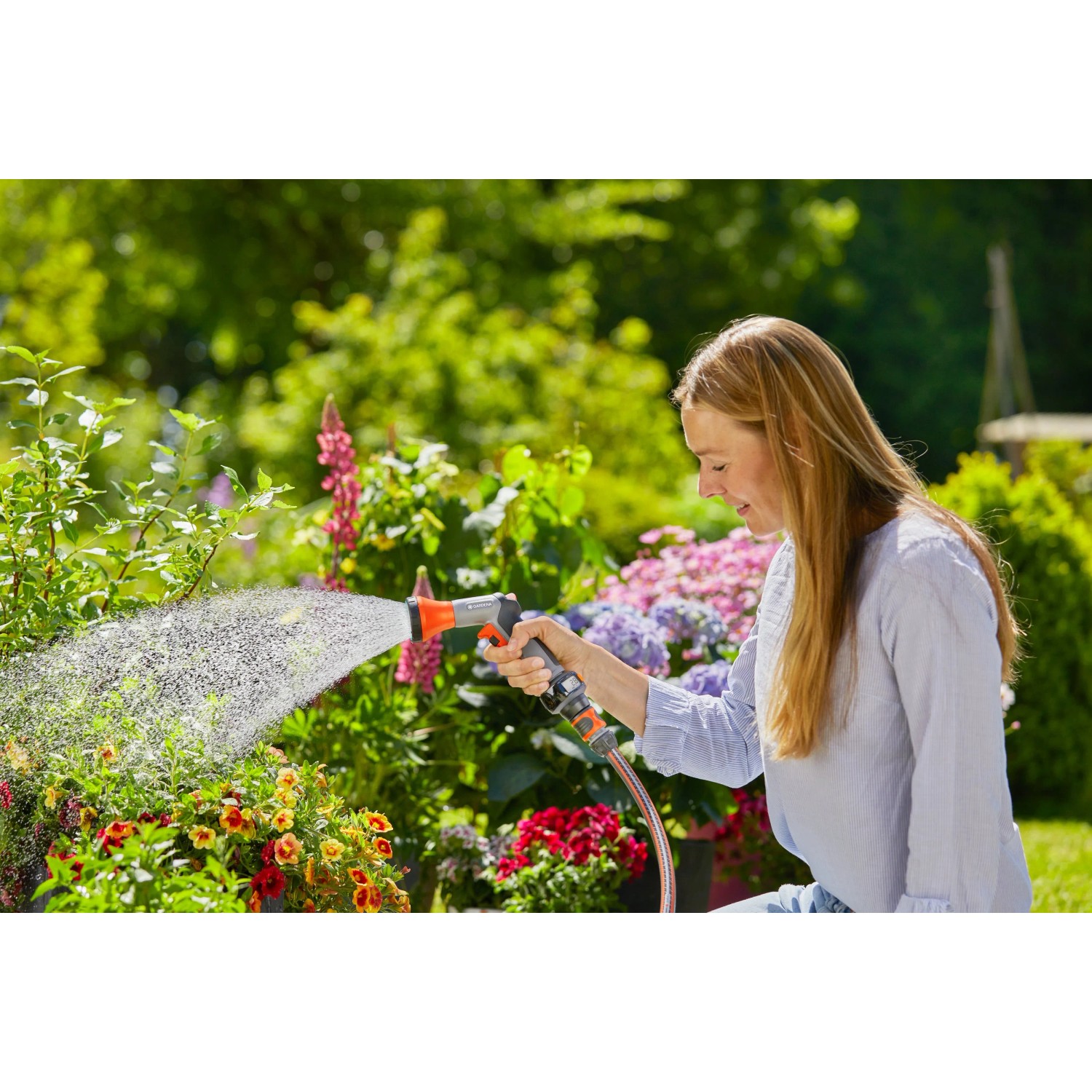 Frau bewässert Blumen mit Gardena Bewässerungsbrause AquaCount im Garten.