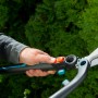 Gardena EnergyCut 2in1 Hand-Heckenschere in Aktion vor grüner Hecke.