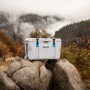 Graue Lifetime Kühlbox Premium (73 Liter) mit blauen Akzenten auf Felsen in der Natur.