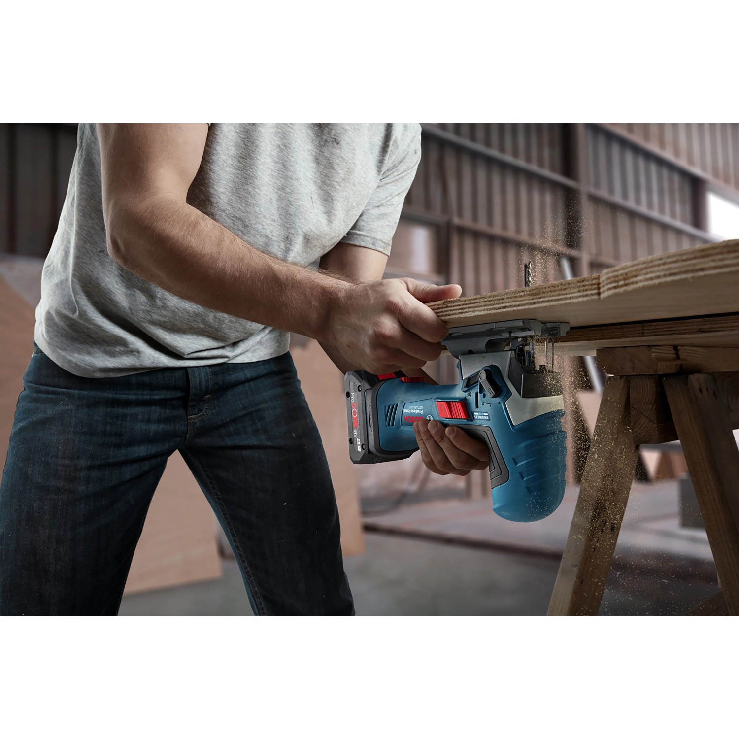 Mann sägt mit blauer Bosch Professional Akku-Stichsäge GST 18 V-125 S ein Holzbrett. Staub fliegt.