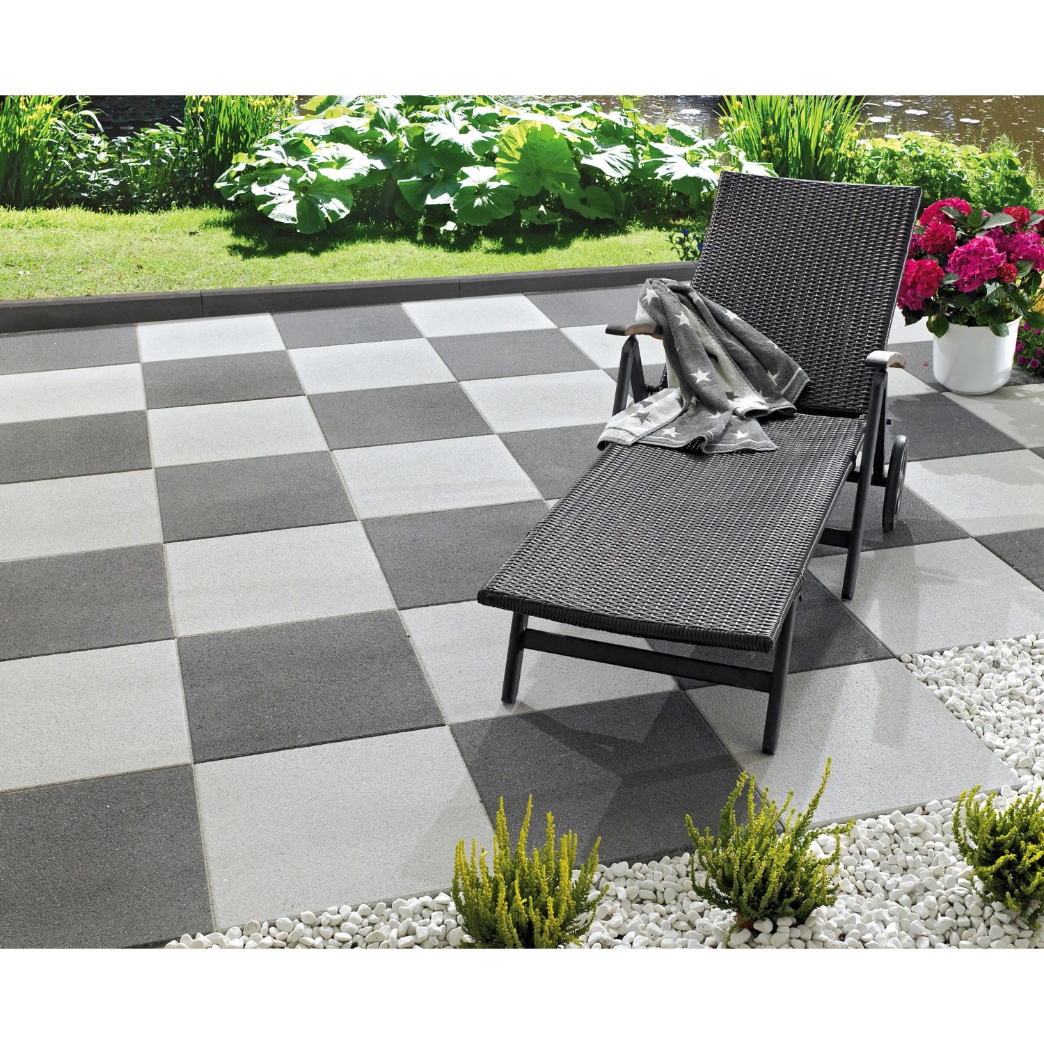 Verlegte, anthrazitfarbene Terrassenplatte Almelo 50x50. Schachbrettmuster mit Liege im Garten.
