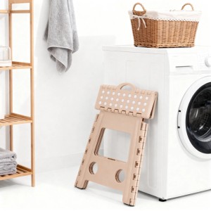 Beiger Relaxdays Klapphocker aus Kunststoff, zusammengeklappt an Waschmaschine. Faltbarer Haushaltshocker mit rutschfesten Punkten.