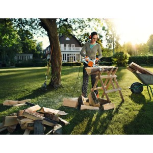Frau sägt Holz mit orange-grauer Stihl Elektro-Motorsäge MSE 141 auf Sägebock im sonnigen Garten.