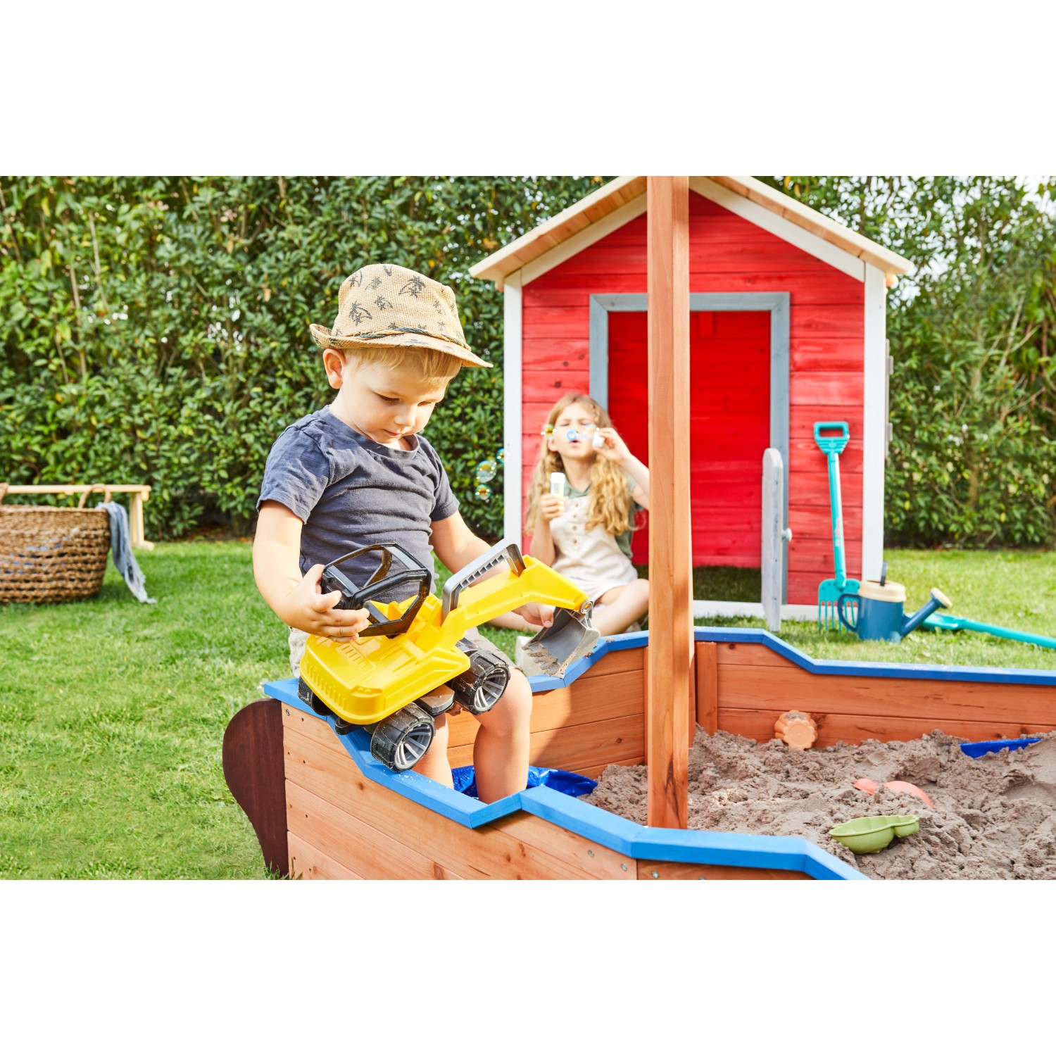 Home Deluxe Sandkasten Matschekiste in Schiffsform mit spielenden Kindern im Garten.