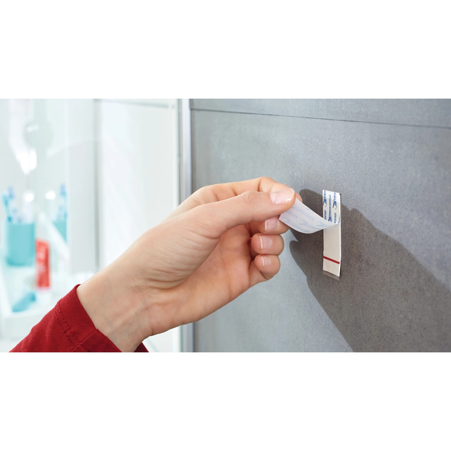 Anbringen eines Tesa Powerstrips Haken Waterproof (Edelstahl, Large) an einer grauen Wand.