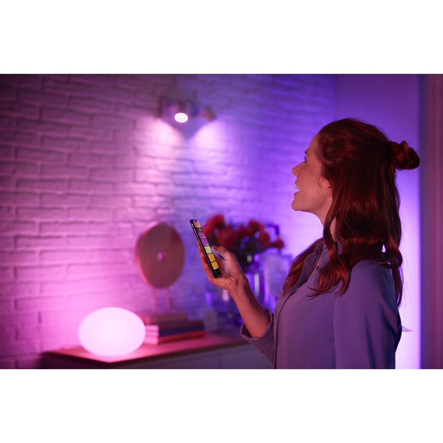 Frau steuert Philips Hue E27 LED Lampe farbig per App.