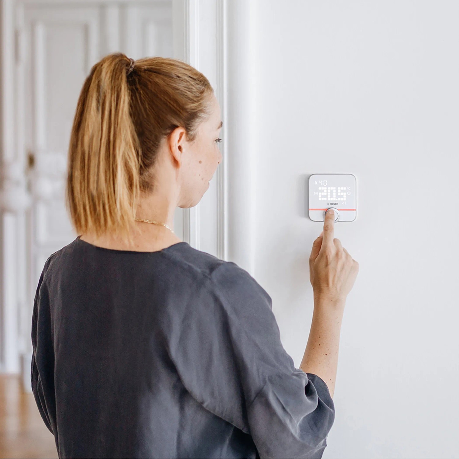 Frau bedient Bosch Smart Home Heizkörperthermostat II zur Temperaturregelung.