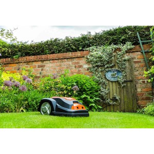 Yard Force Mähroboter SA650B auf Rasen vor Gartenmauer und Holztür.