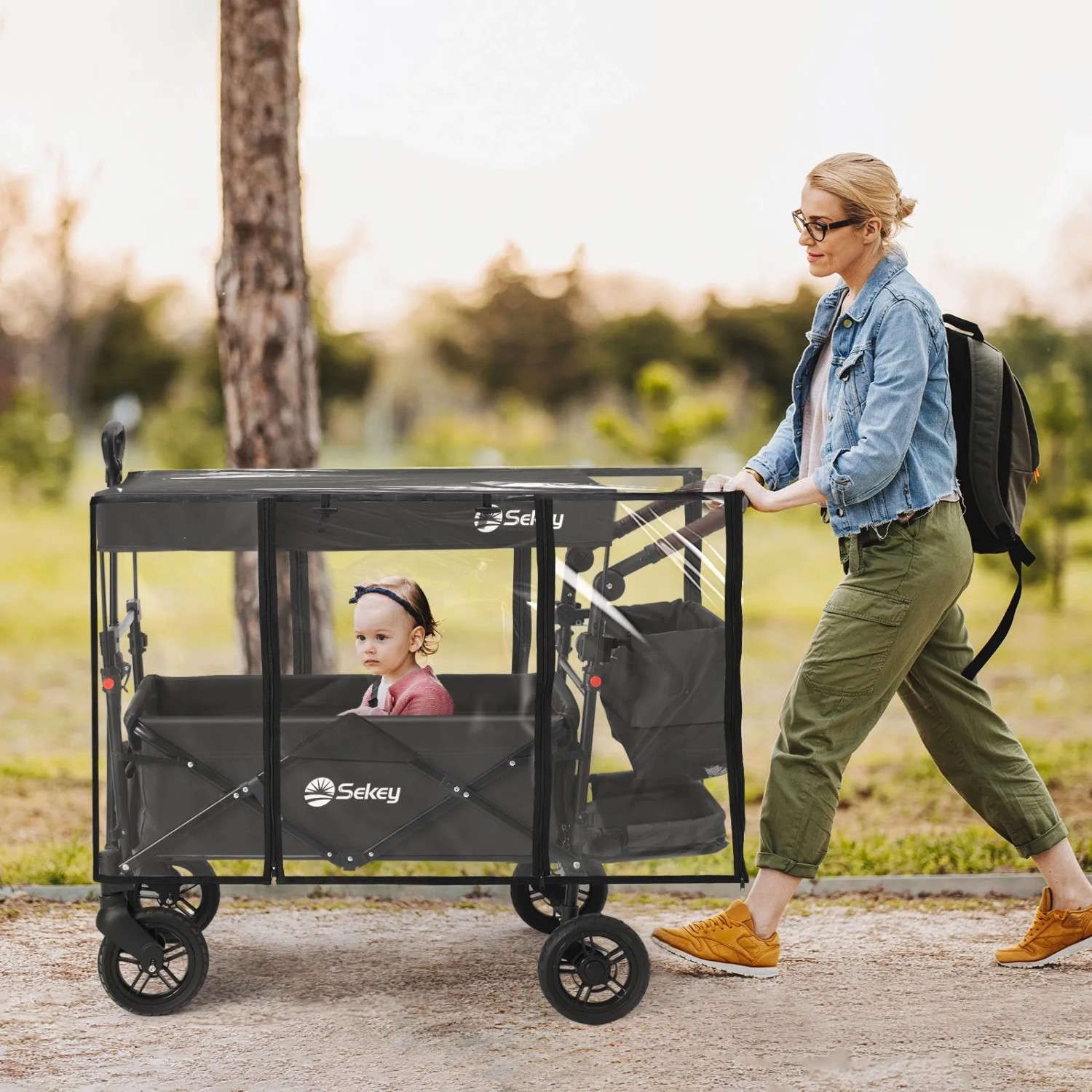 Sekey Bollerwagen mit Regenschutzhülle, transparent, mit Kind und schiebender Person.