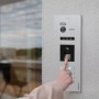 Silber-schwarze Balter EVO-HD Video-Türstation mit Fingerprint-Sensor an Wand. Hand drückt Sensor für schlüssellosen Zugang.