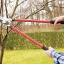 LUX Amboss Astschere in Nutzung: Eine Hand schneidet einen Ast. Gartenschere mit roten Griffen.